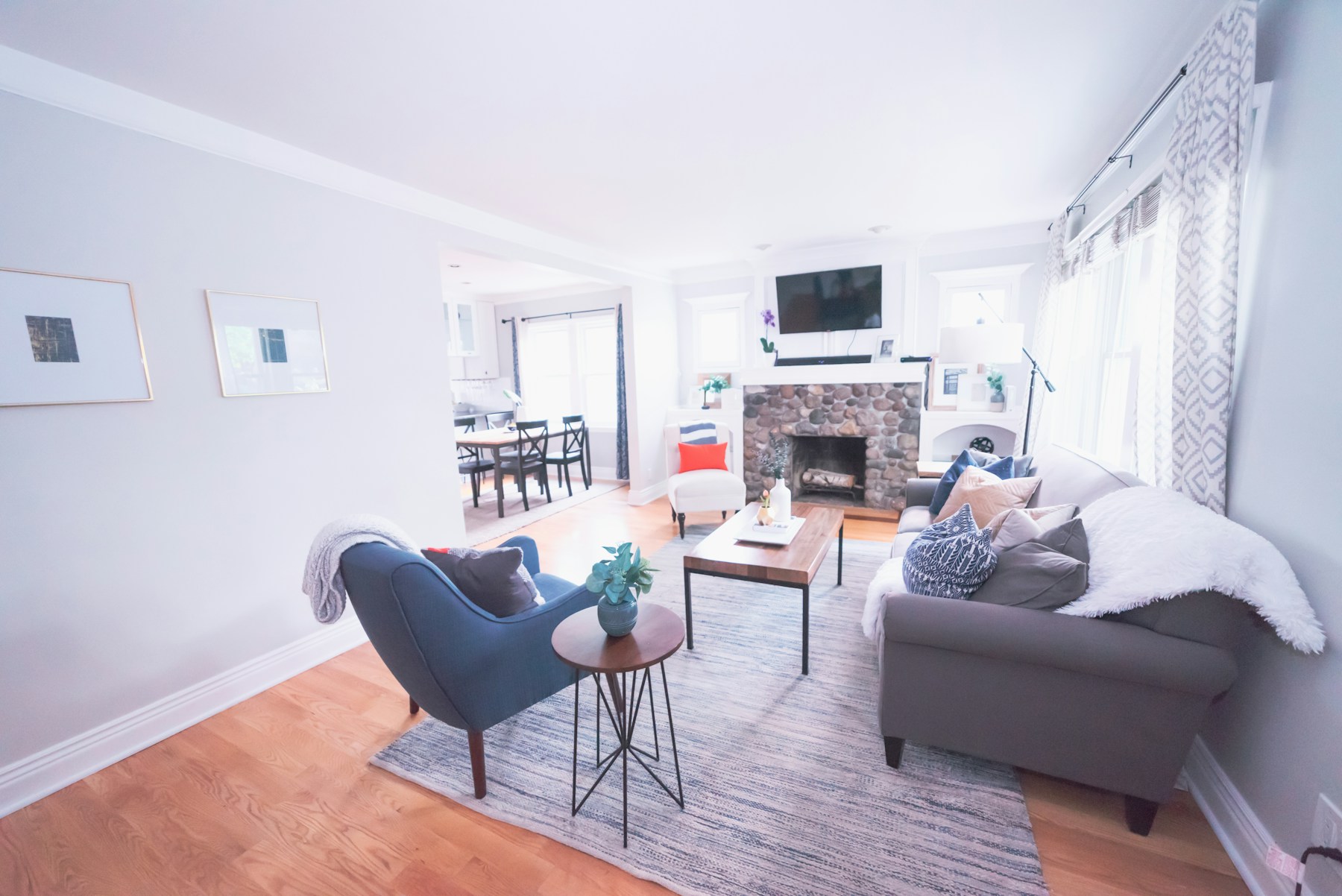 A bright living room with a stone fireplace, white walls and a blue armchair